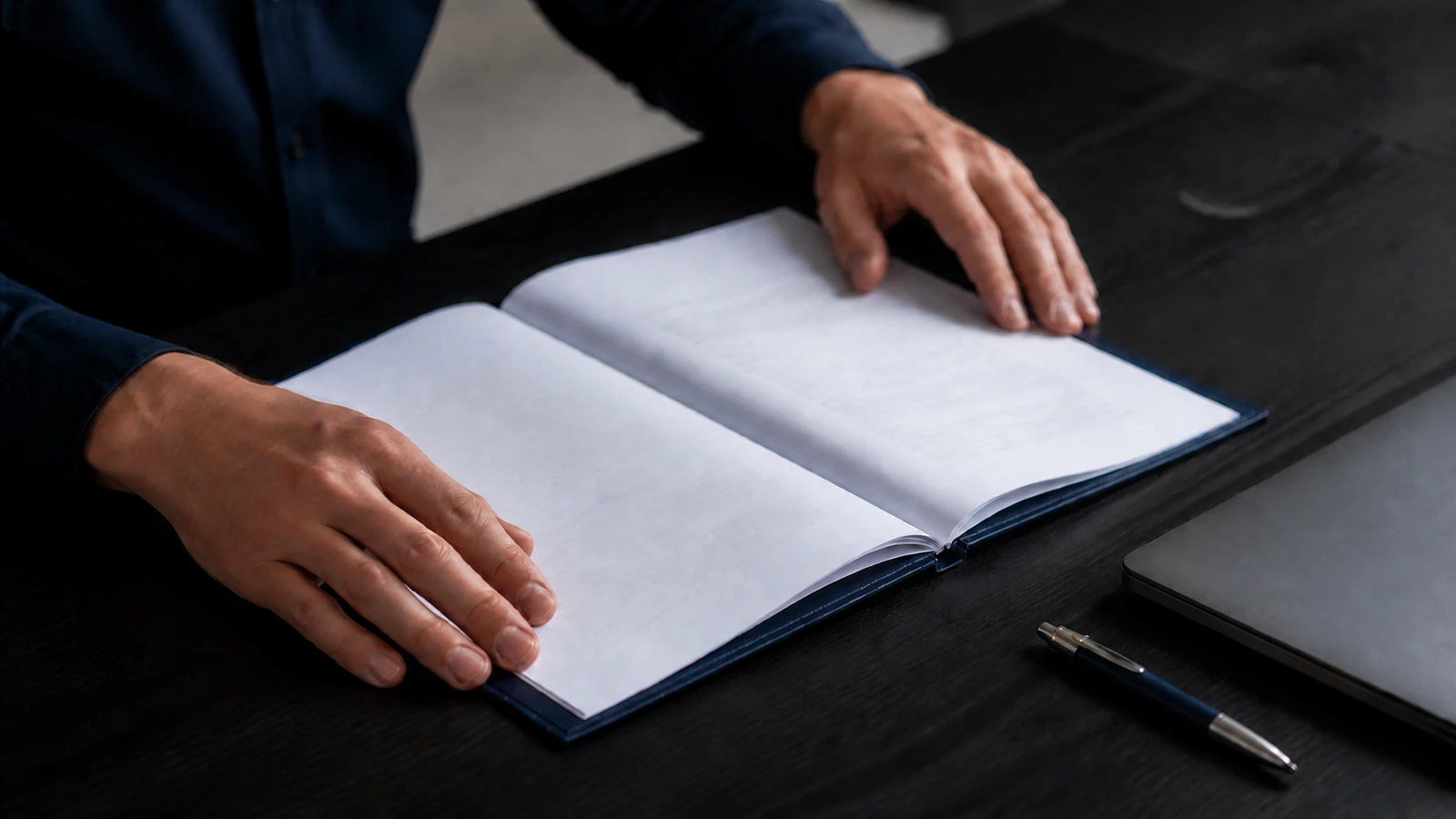 Hands reviewing a bound contract document beside a laptop on a desk