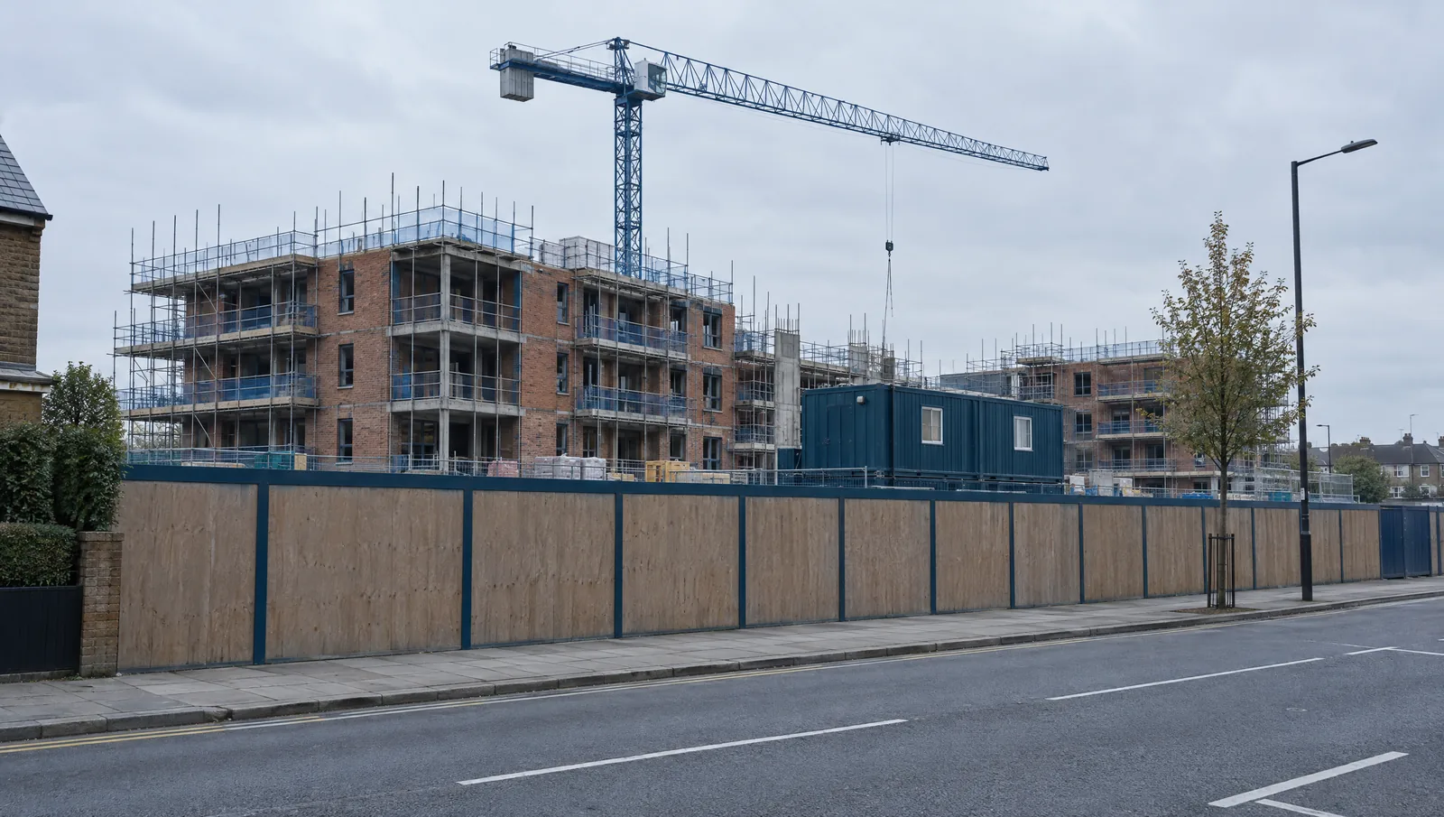 Residential scheme under construction behind site hoarding, with scaffolding and a tower crane